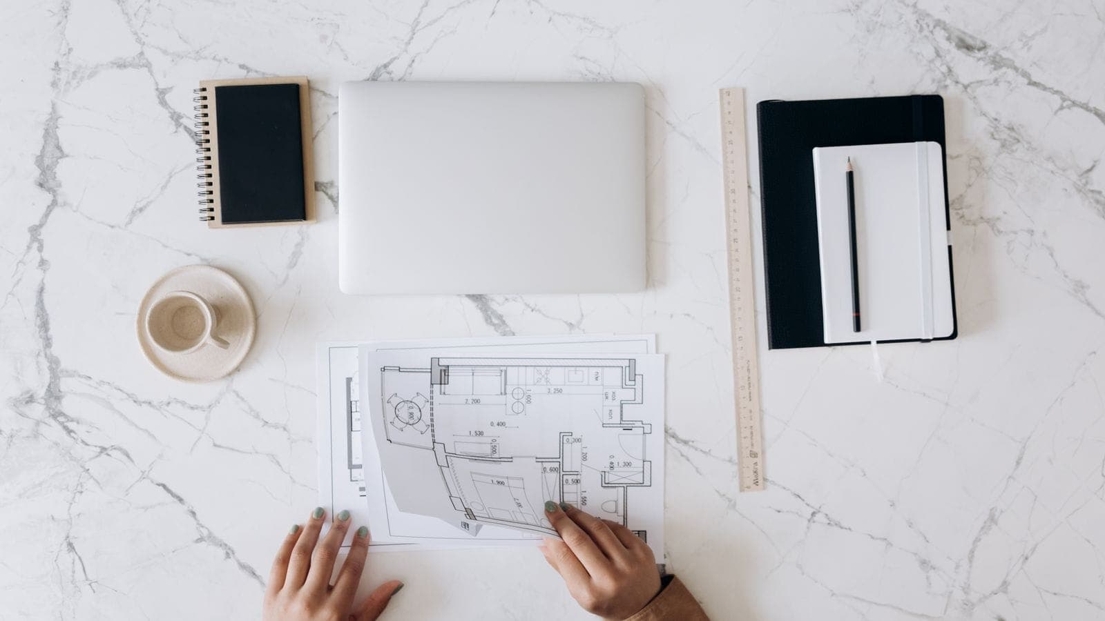 Overhead flat lay of an architect's workspace with blueprints, a laptop and a notebook