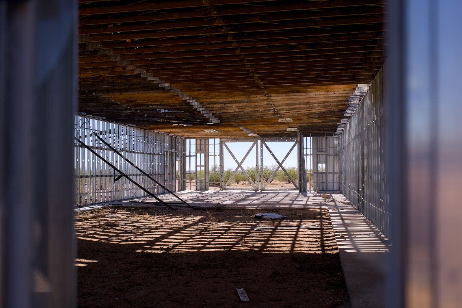Interior of an unfinished commercial building with metal stud framing and exposed roof joists in bright sunlight