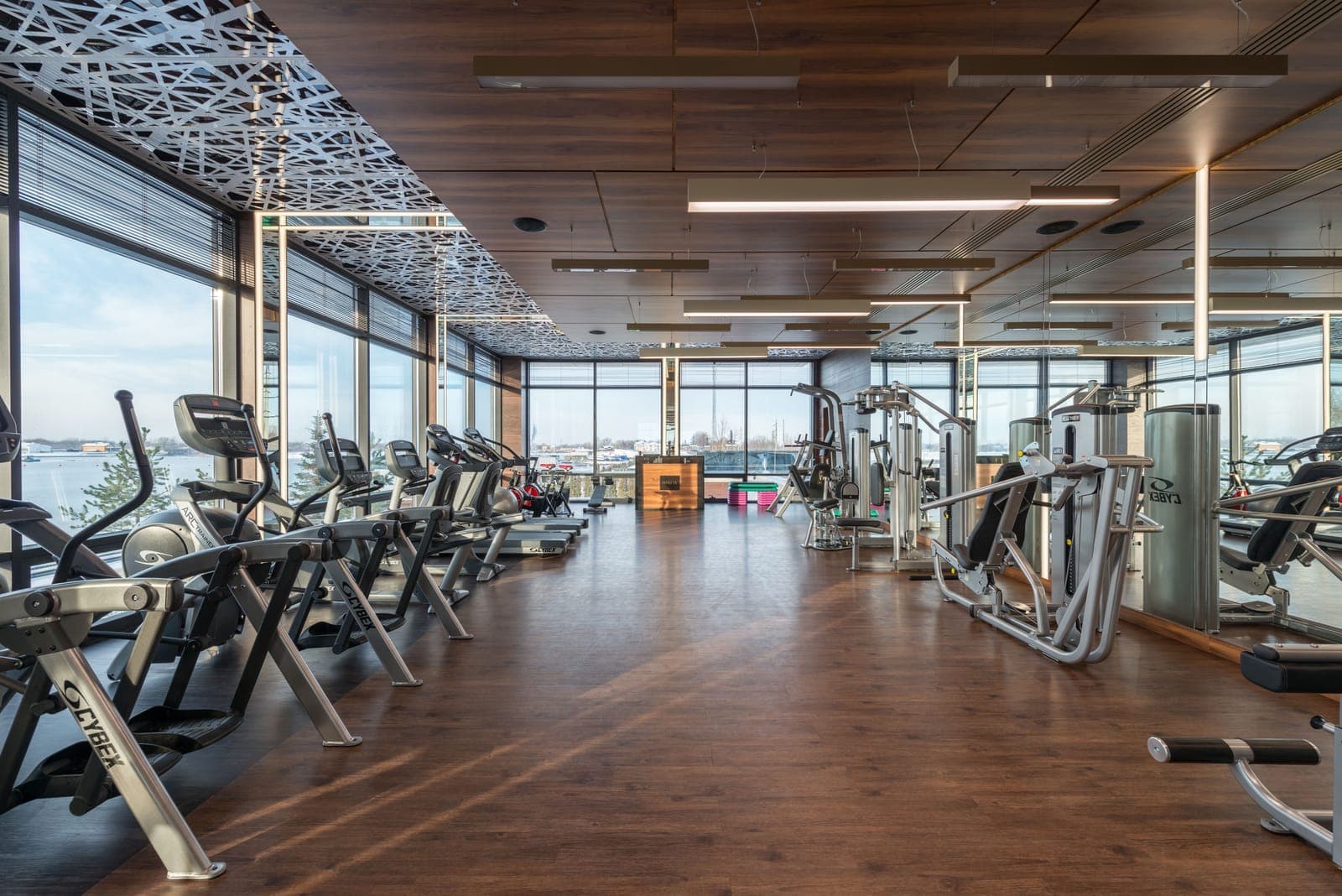 Interior of a modern fitness club with rows of exercise machines near large windows