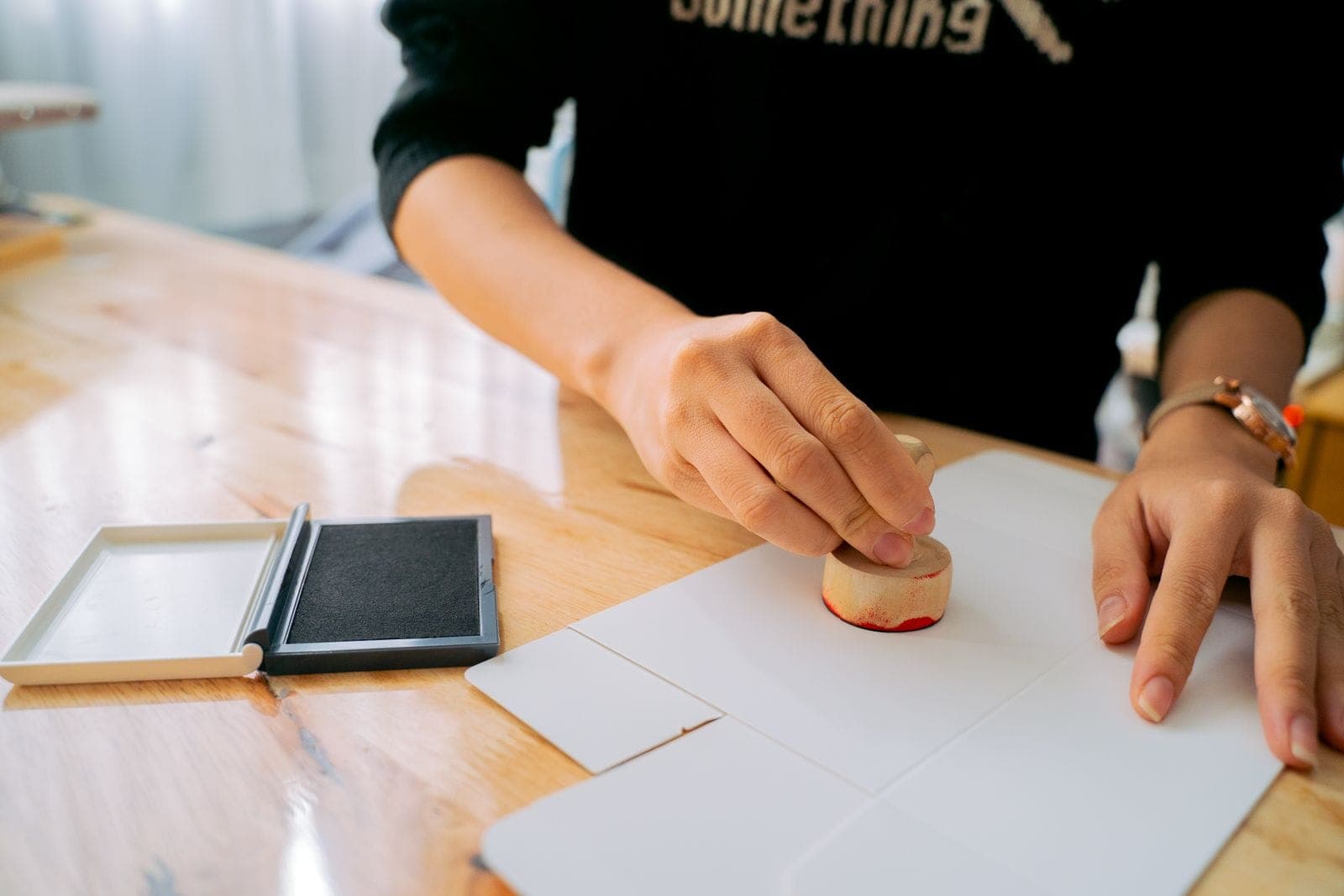 A hand pressing a rubber stamp onto a paper document on a desk