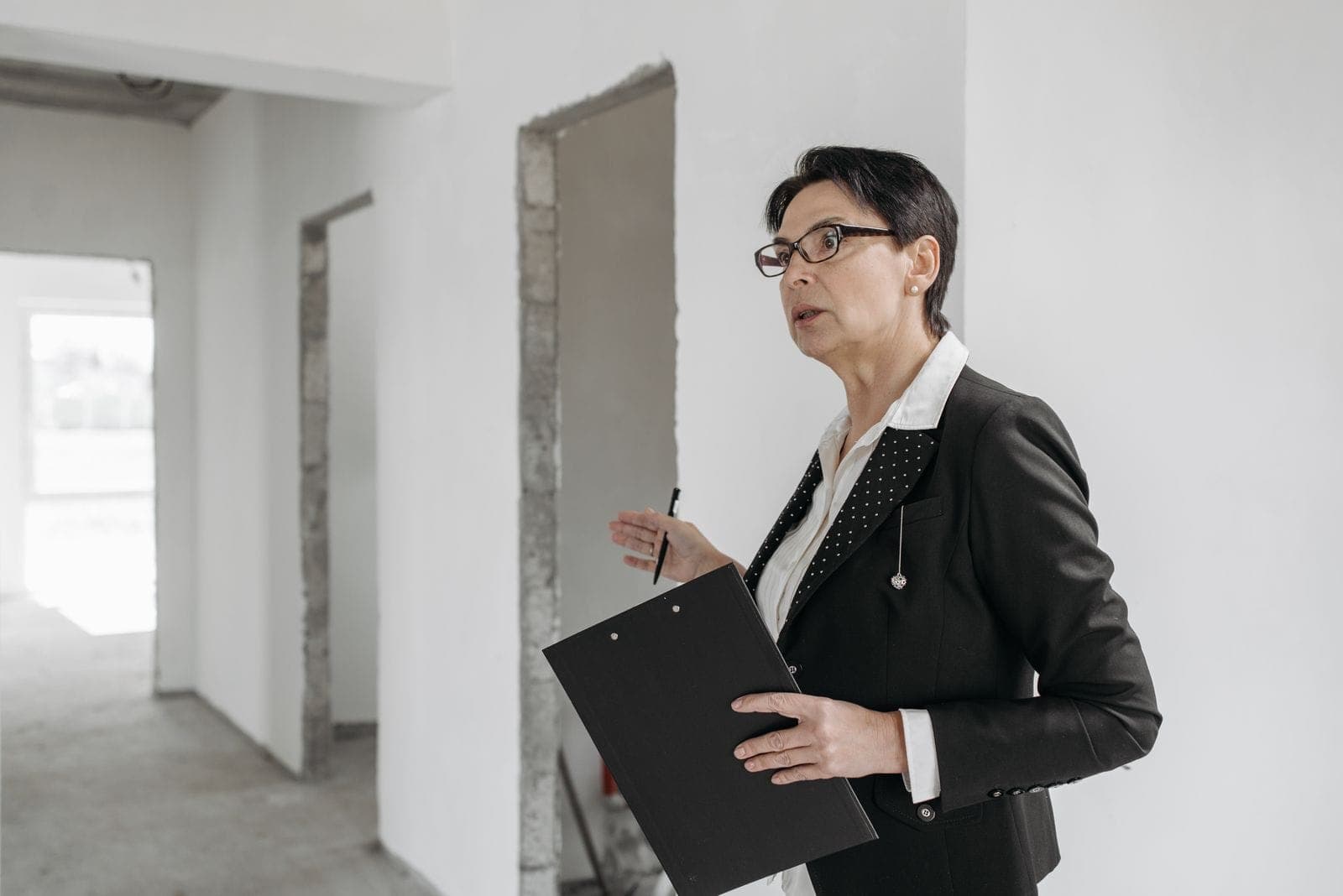 A woman in a suit holding a clipboard, inspecting an unfinished interior construction site