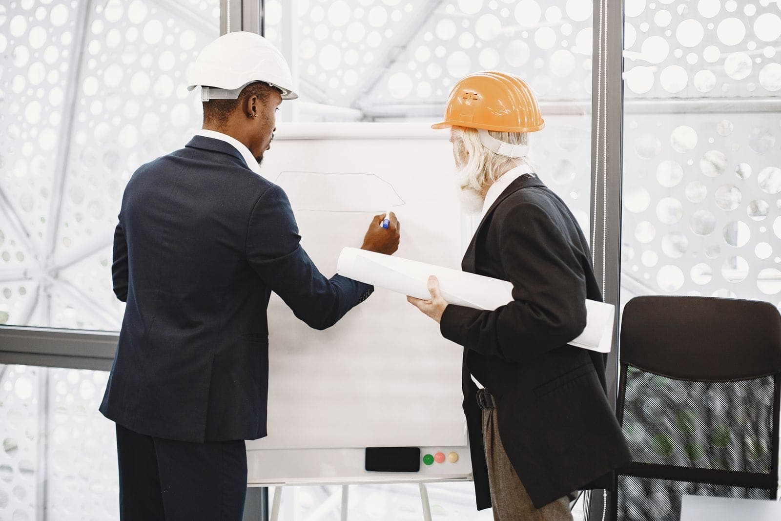 Two people in hard hats reviewing construction plans together over a table
