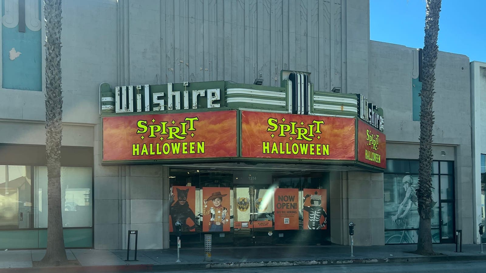 A Spirit Halloween store in the old Wilshire Theatre in Santa Monica, with orange Spirit Halloween banners across the Art Deco marquee and costume posters and a Now Open sign in the entry