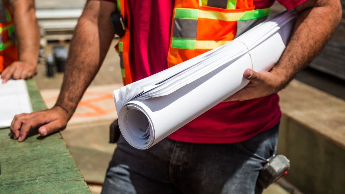 Construction workers in high-visibility vests holding a rolled set of drawings on site