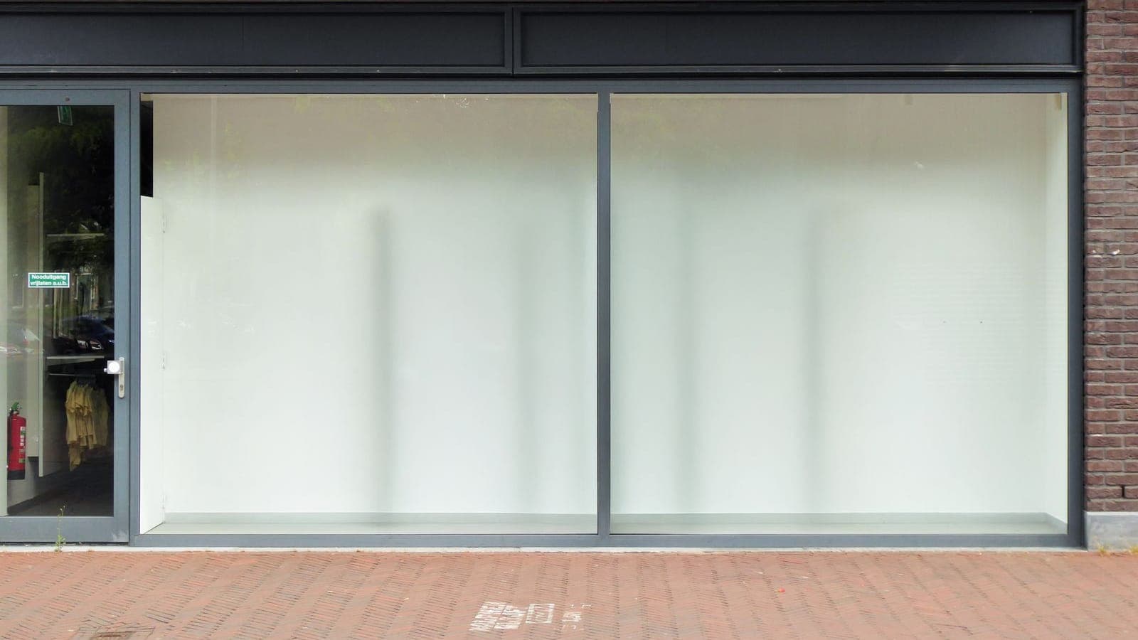 Empty retail storefront with large glass display windows papered white and a glass entry door, a shop between fit-out and opening